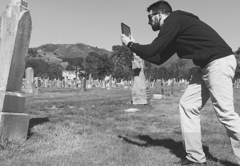 Picture of a man taking a photo of a headstone with a tablet